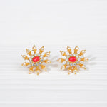 Gold-toned floral stud earrings with red stone, pearls, and clear gemstones on white background