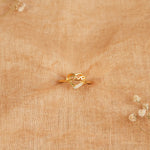 Gold heart-shaped designer ring with cubic zirconia accents on beige fabric background