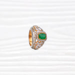 Gold and silver ring with green gemstone center and floral diamond accents on white background