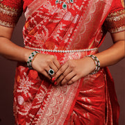 Woman wearing red silk saree with silver jewelry, emerald ring, and gemstone bangles