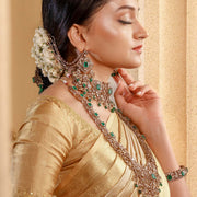 Woman in gold saree wearing traditional silver and green gemstone earrings and necklace set